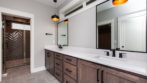 bathroom with two vanities, stained wood cabinets, white stone countertops, looking into shower with grey glass tile