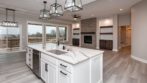 hanging pendant lights over white stone counter and white cabinets, overlooking living area with stacked stone fireplace and large wall of windows