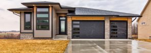 front of modern looking home with tan siding, black garage doors with windows and horizontal stacked windows