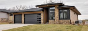 modern home exterior with stone facade front, modern garage doors with windows and tan siding