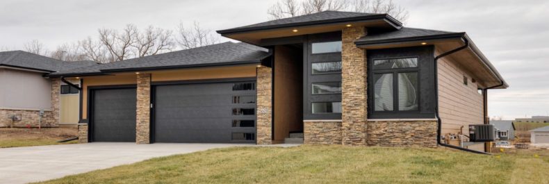 modern home exterior with stone facade front, modern garage doors with windows and tan siding
