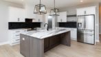 light blonde wood floors, white cabinets, black back splash, stainless steel appliances, white and gray marble countertops and hanging black iron light fixtures