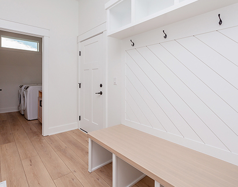 Black House Entryway mudroom with light wood bench, coat hooks, light wood plank floors leading into laundry room