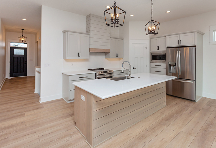 Black House Kitchen kitchen with light wood flooring, light wood and taupe cabinetry, white counter and stainless steel appliances