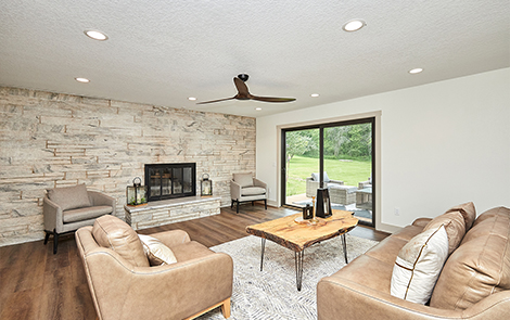 living area with large stone accent wall with built-in fireplace, tan couches and raw rustic wood coffee table