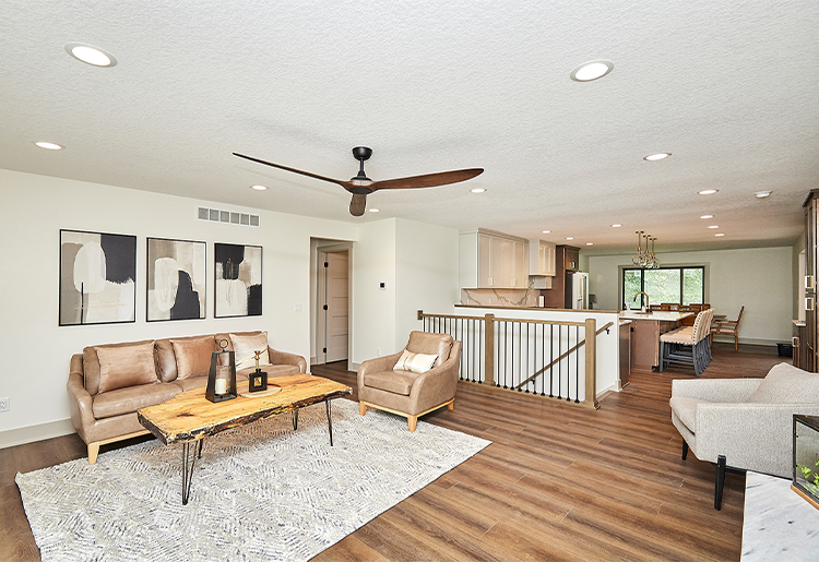 tan couches and raw rustic wood coffee table, white patterned rug, railing to stairs, looking into kitchen